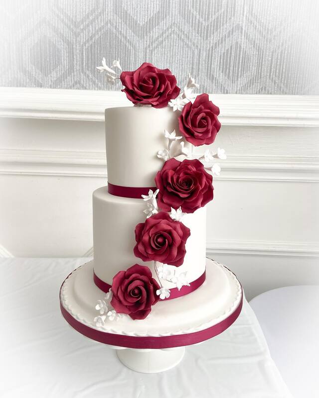 Stunning 2 tier white wedding cake decorated with cascading deep burgundy sugar roses and white blossom flowers