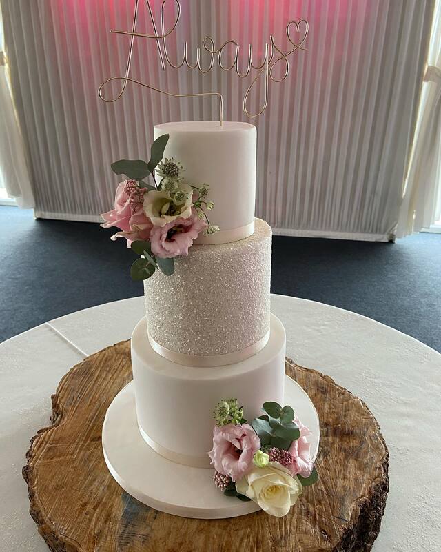 3 tier elegant white wedding cake with middle glitter tier and decorated with beautiful fresh flowers