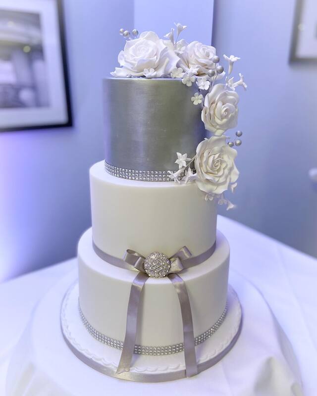 stunning silver and white 3 tier wedding cake decorated with diamante ribbon and brooch and beautiful handmade white sugar roses and blossoms