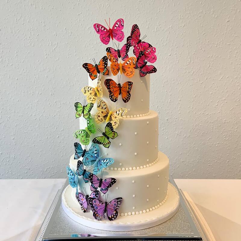 a colourful 3 tier wedding cake with a rainbow pride cascade of beautiful butterflies