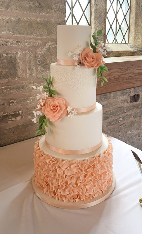 beautiful 4 tier luxury wedding cake with peach ruffles bottom tier and peach sugar roses with white blossom flowers and green foliage