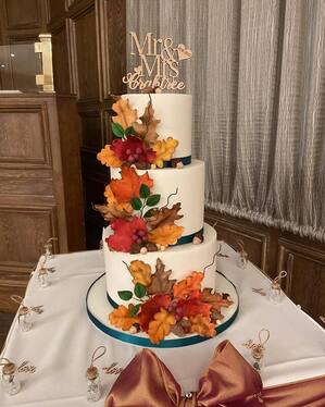 Autumnal themed 3 tier wedding cake decorated with various sugar autumn leaves of golds reds oranges and brown with acorns