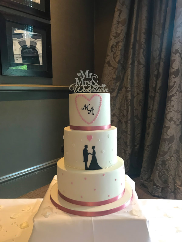 an elegant white and dusky pink wedding cake with a bride and groom silhouette and initials decorated with mini lovehearts